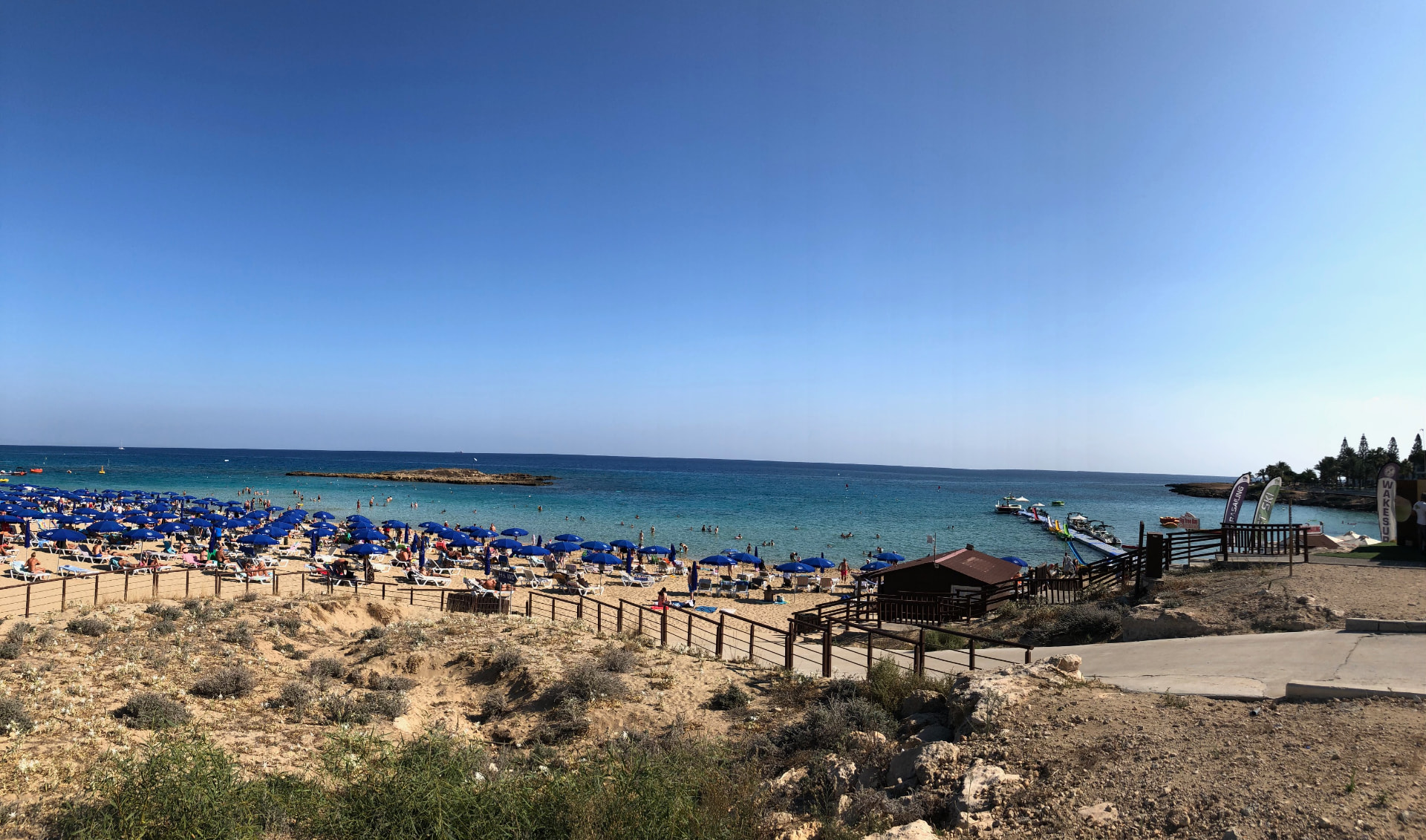 Busy Fig Tree Bay beach with blue umbrellas, turquoise water and a clear summer sky