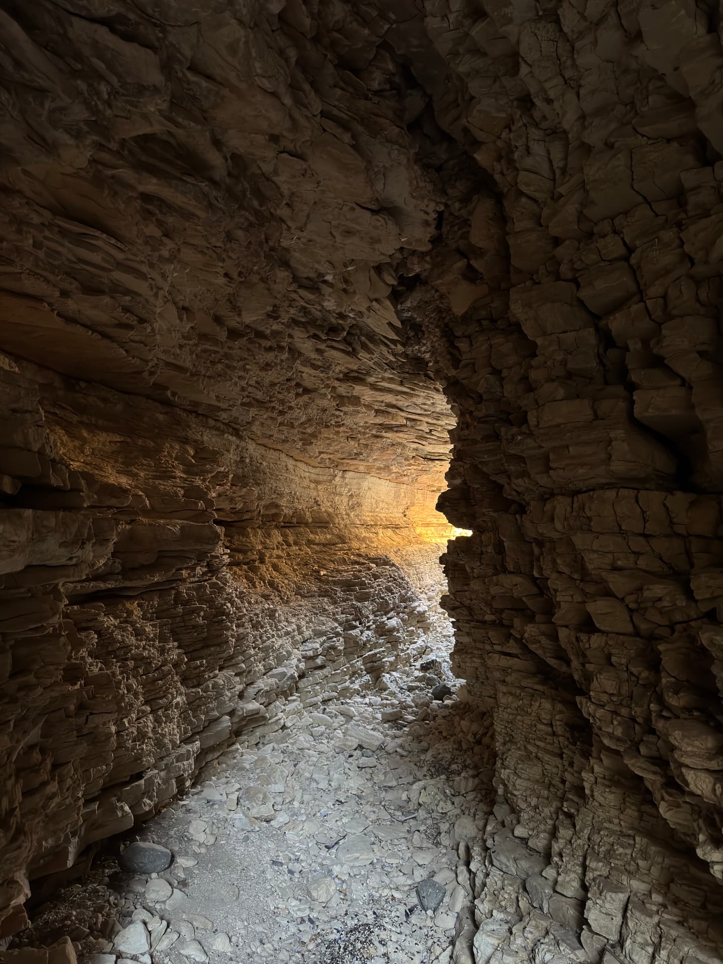 Golden evening light spilling through a narrow gap in the rock into the dark cave passage