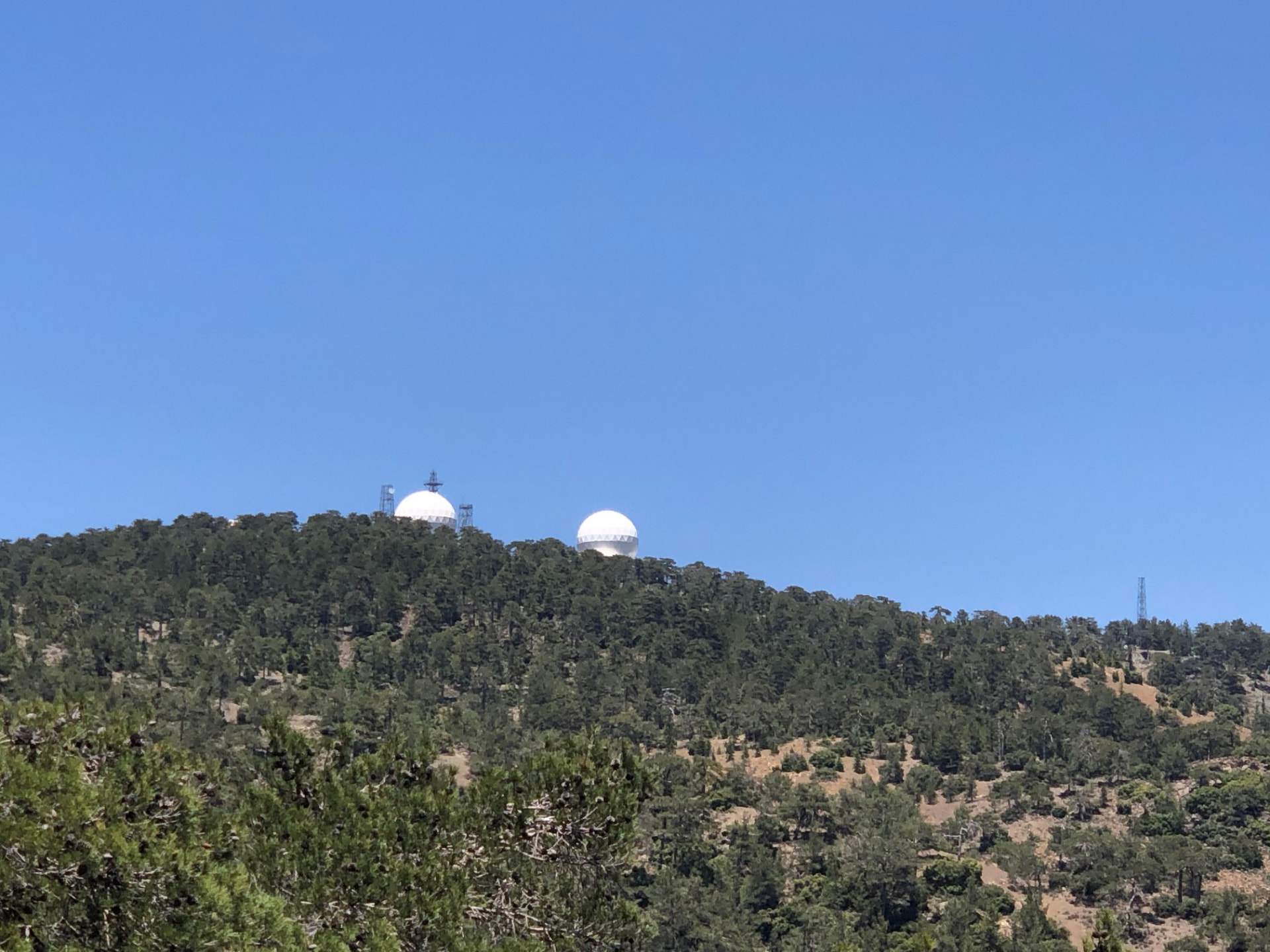White radar domes on top of a forested hill against a clear sky