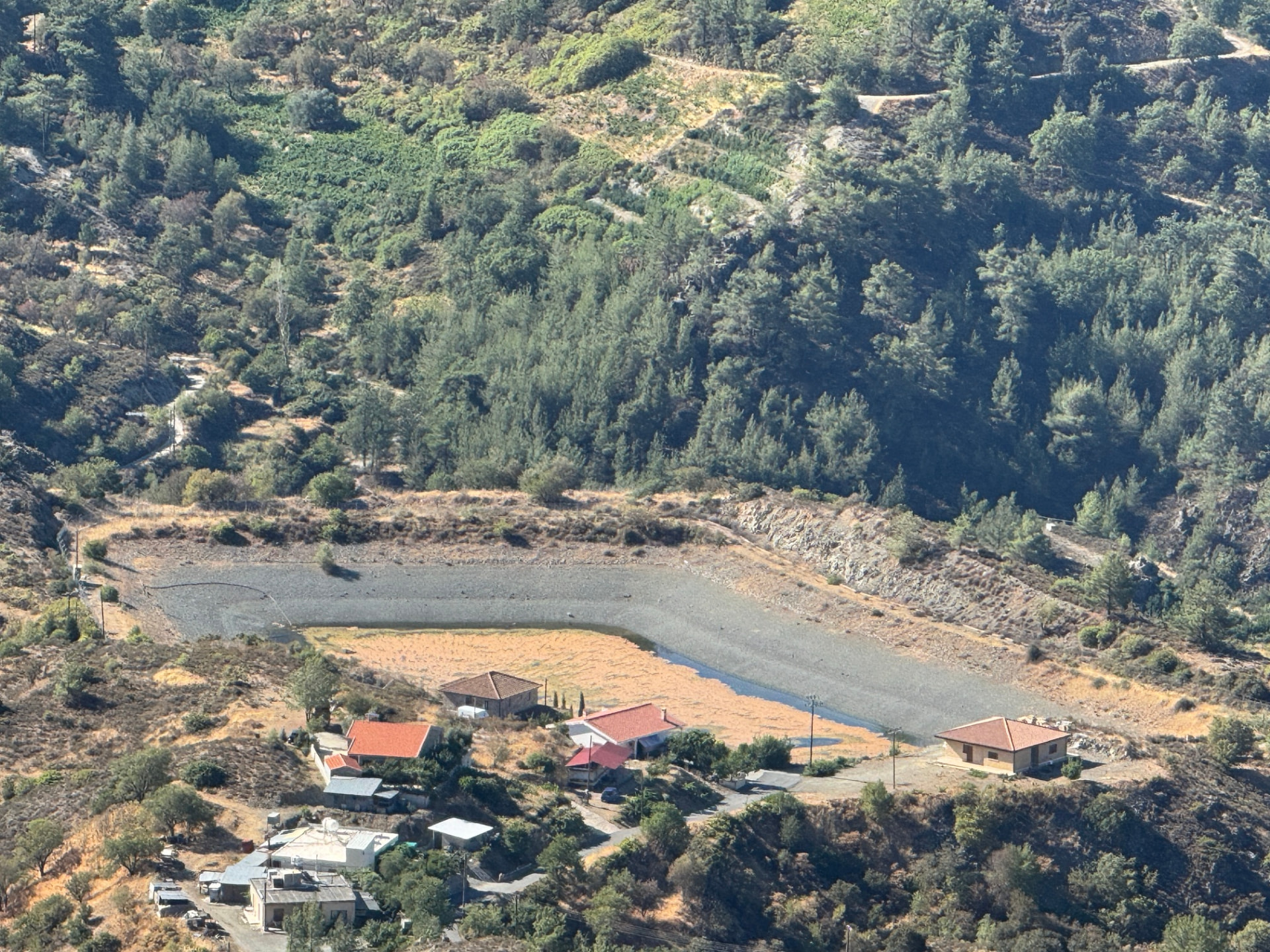 Village houses with red roofs and a nearly dry reservoir seen from high above