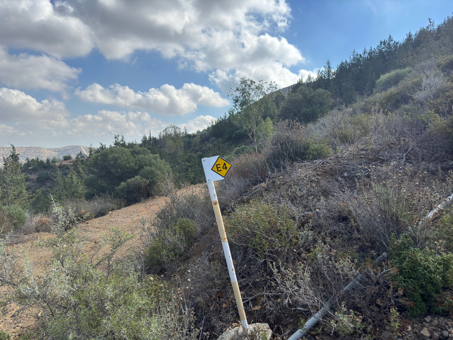 A small E4 sign on a dusty track beside dry shrubs