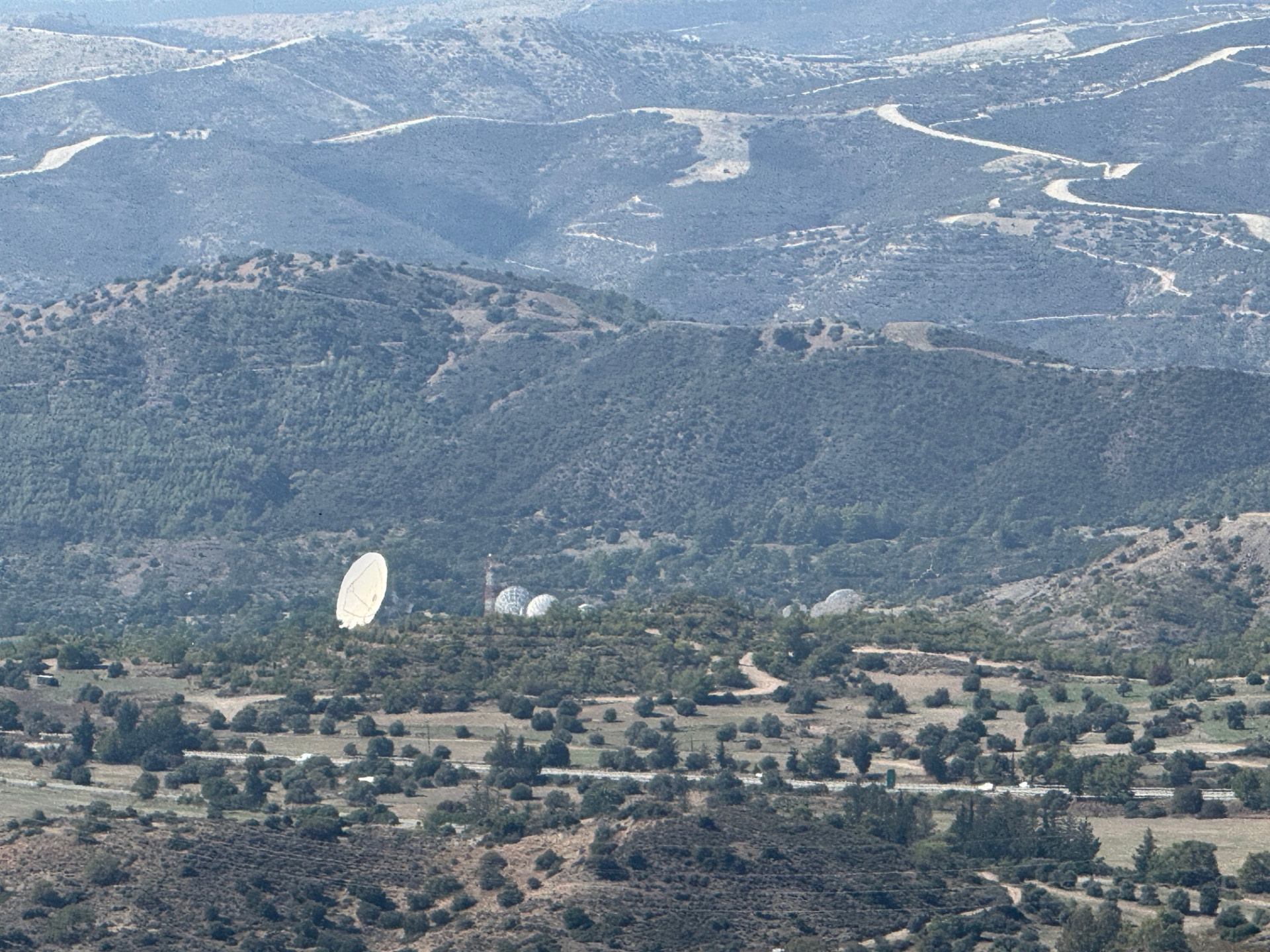 A white satellite dish and radar domes hidden in distant hills
