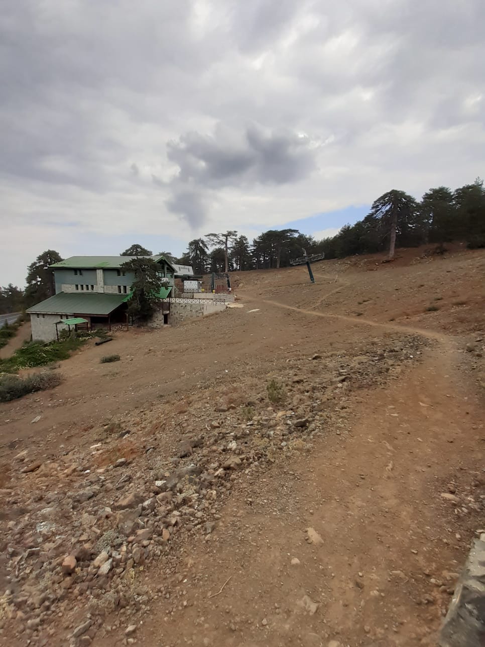 Open rocky slope with a green-roofed building and a ski lift under heavy clouds