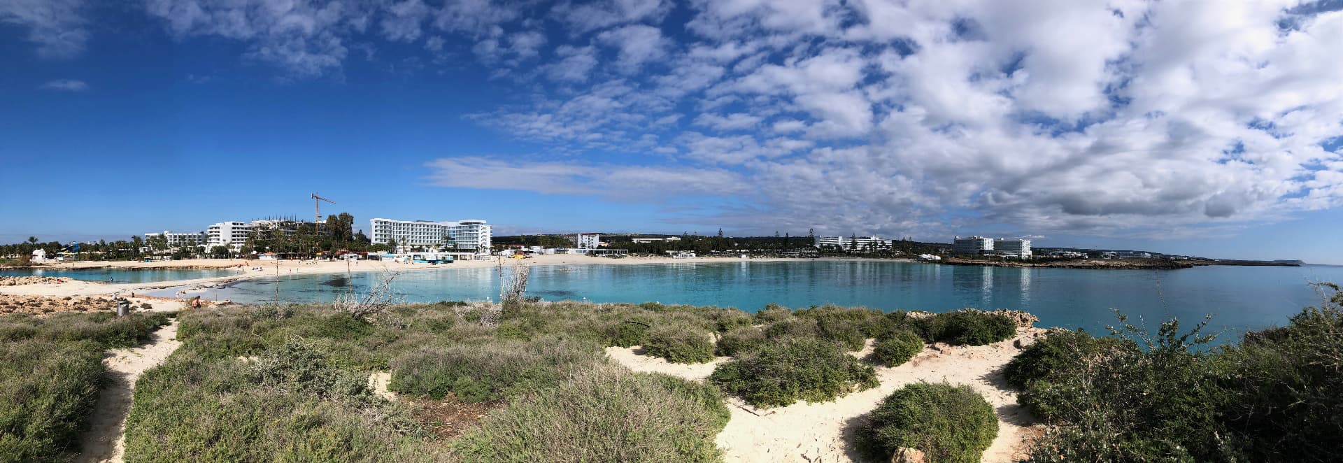 Panoramic view of Nissi Beach with turquoise water, white sand and coastal hotels under a bright blue sky