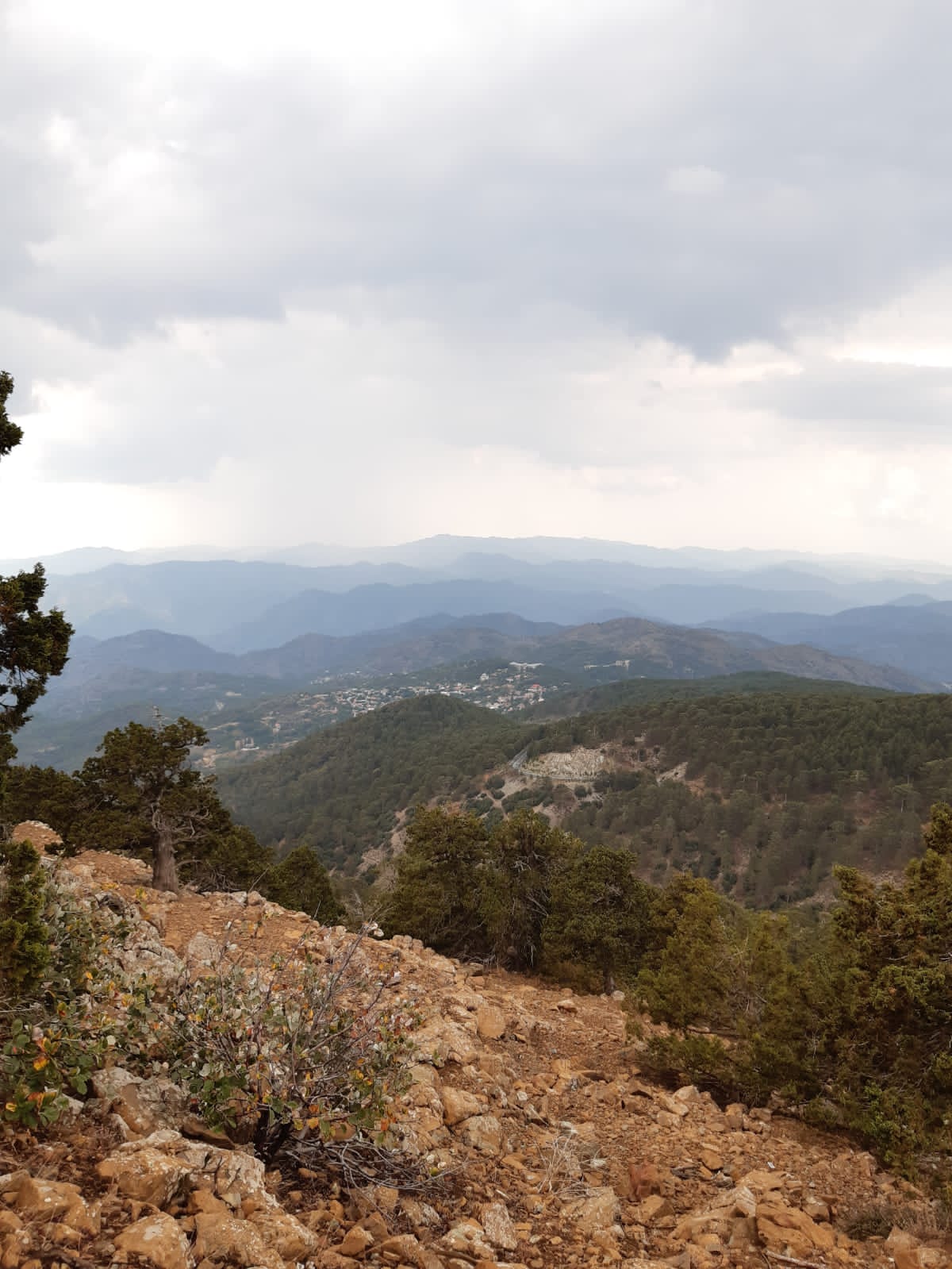 Rocky foreground overlooking pine-covered hills and a distant village