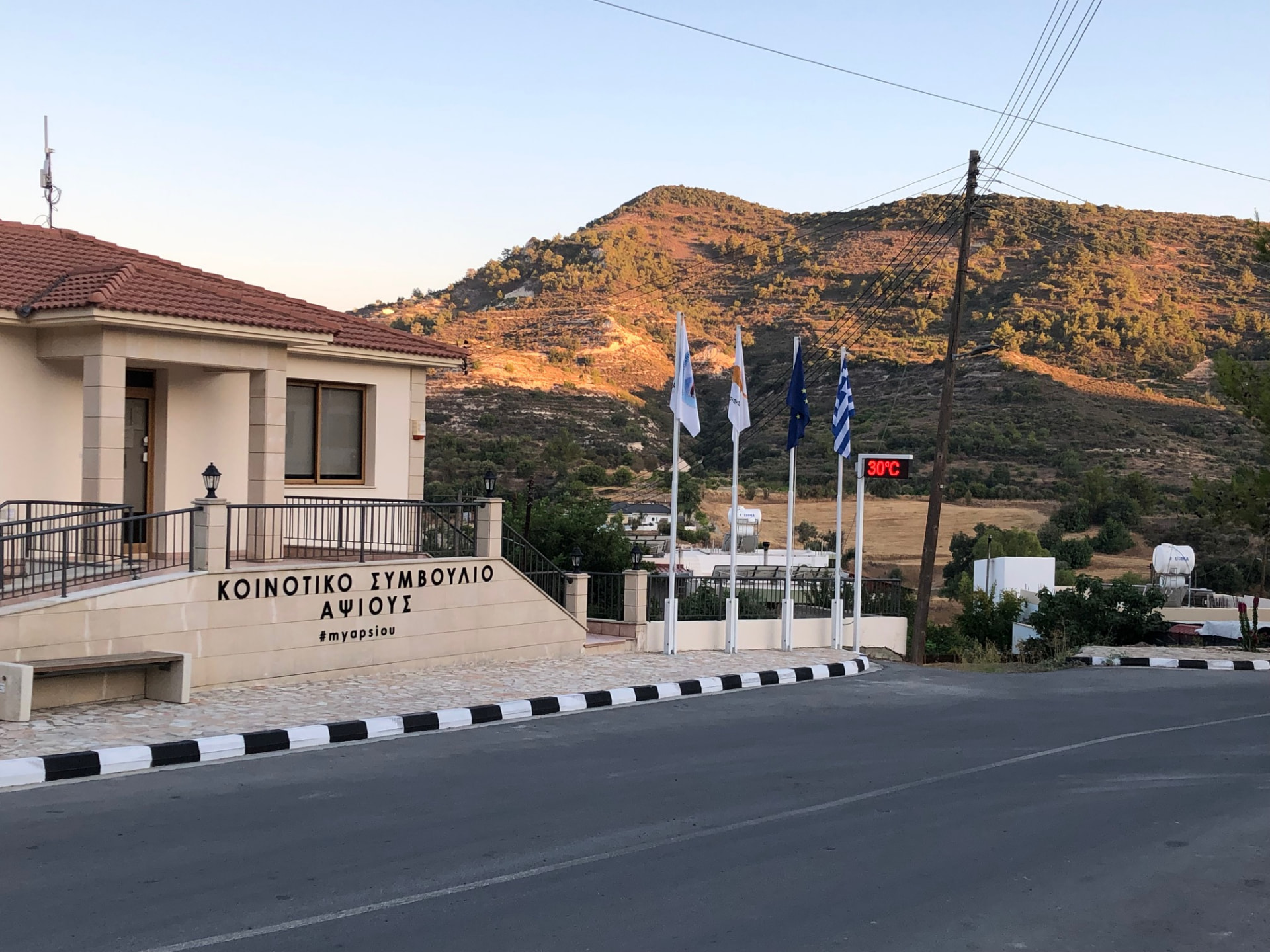 Apsiou village community council building with mountains in the background and a 30°C sign