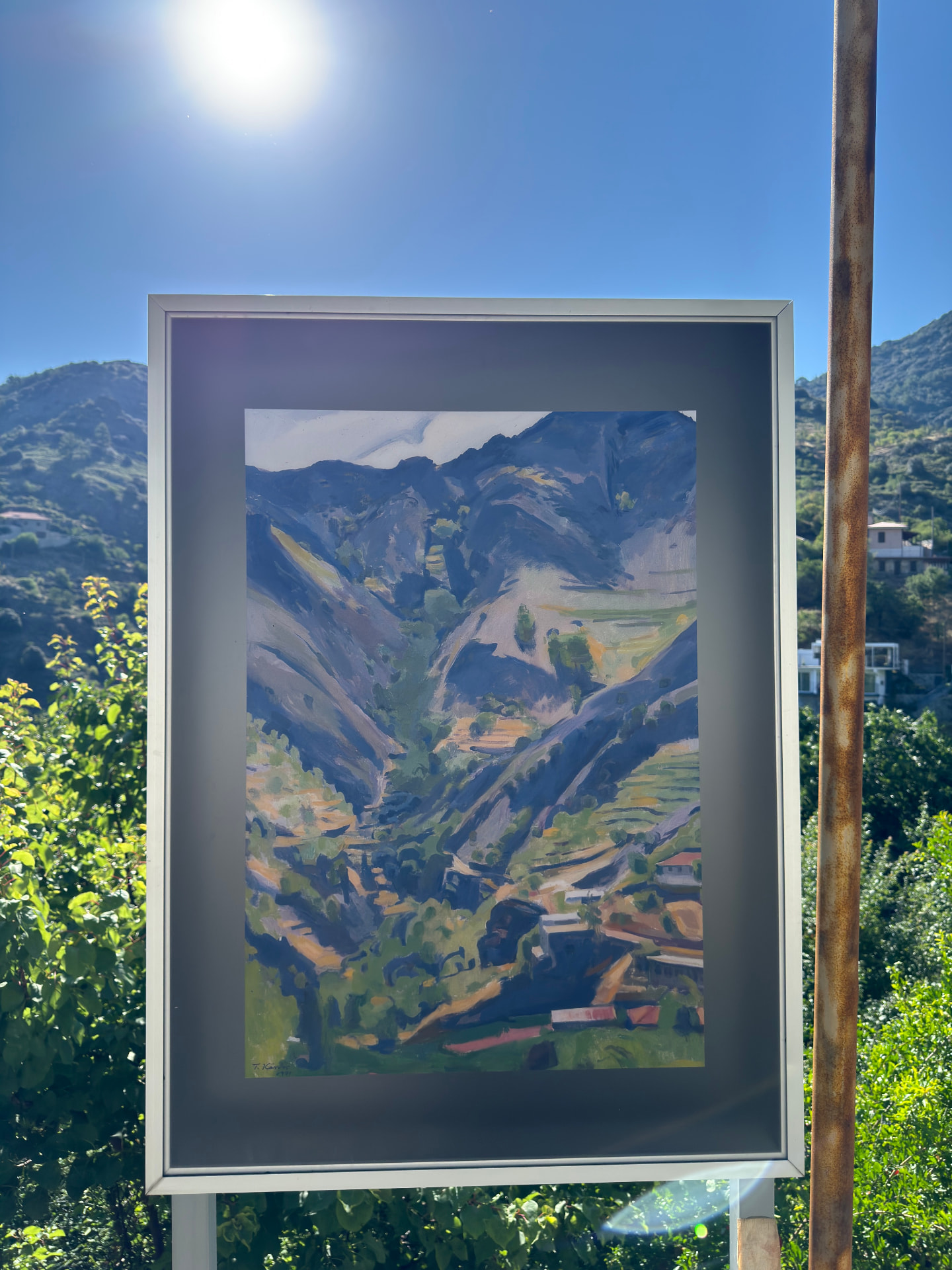 A framed landscape painting with real mountains behind it