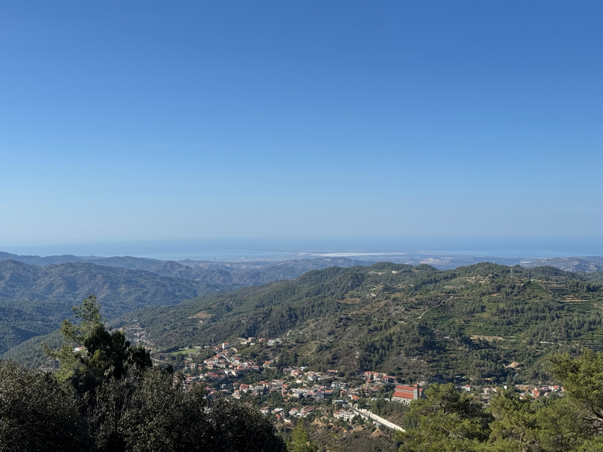 Terraced hillsides with a village of red roofs in the valley and the coastline in the distance