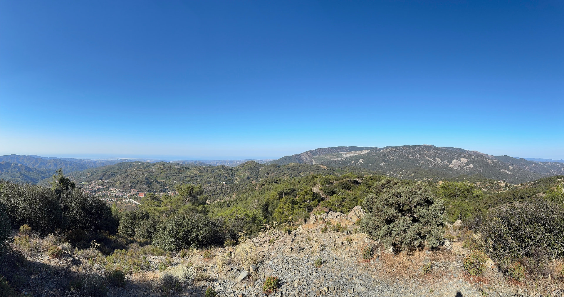A panoramic view from the ridge with rocky foreground, forested hills and the sea on the horizon