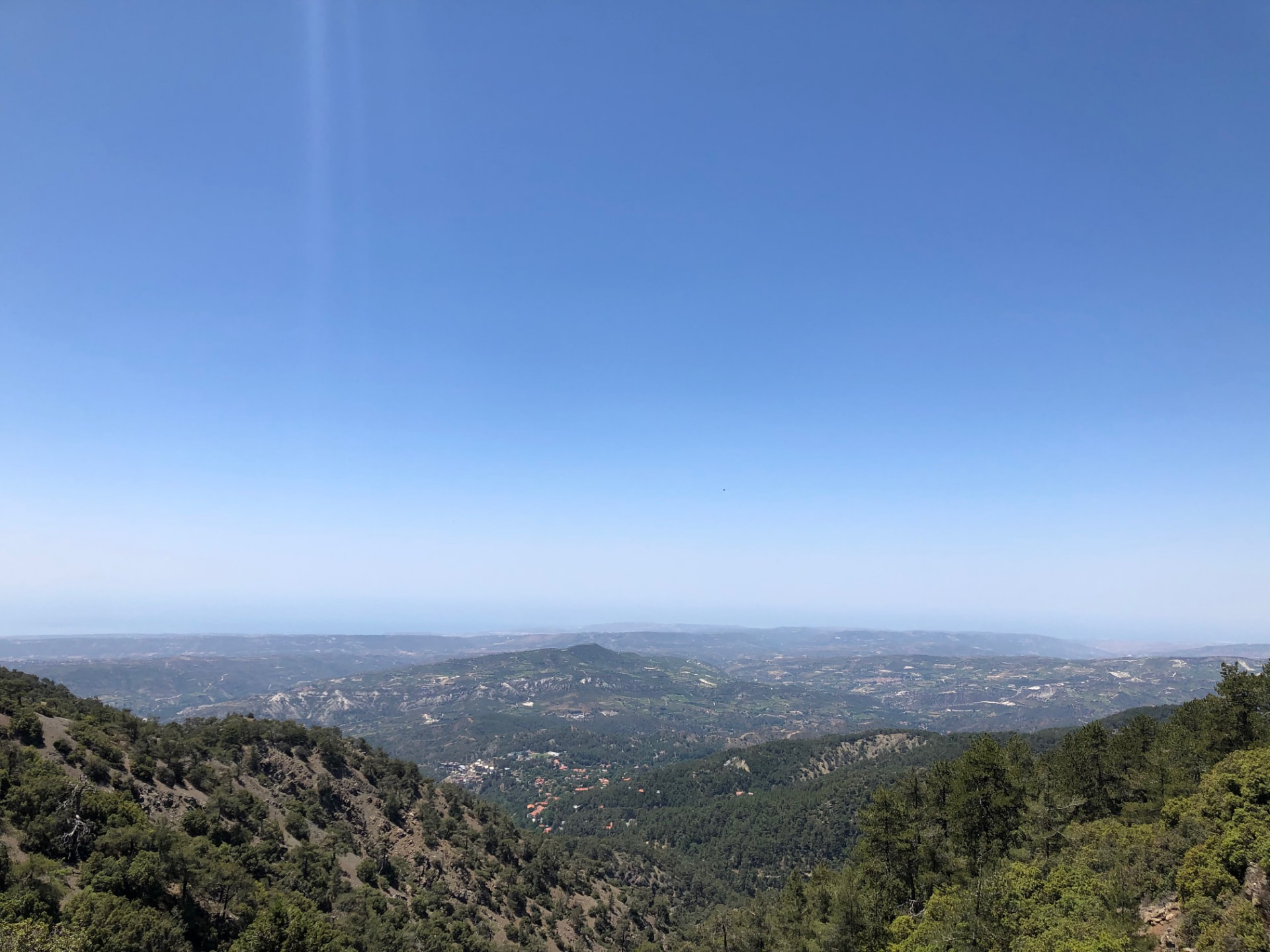 Forested mountainsides falling away toward a hazy plain under blue sky