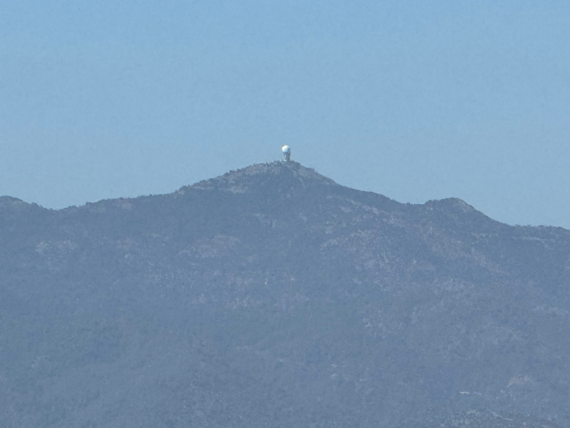 A hazy mountain ridge with a small radar dome on its peak