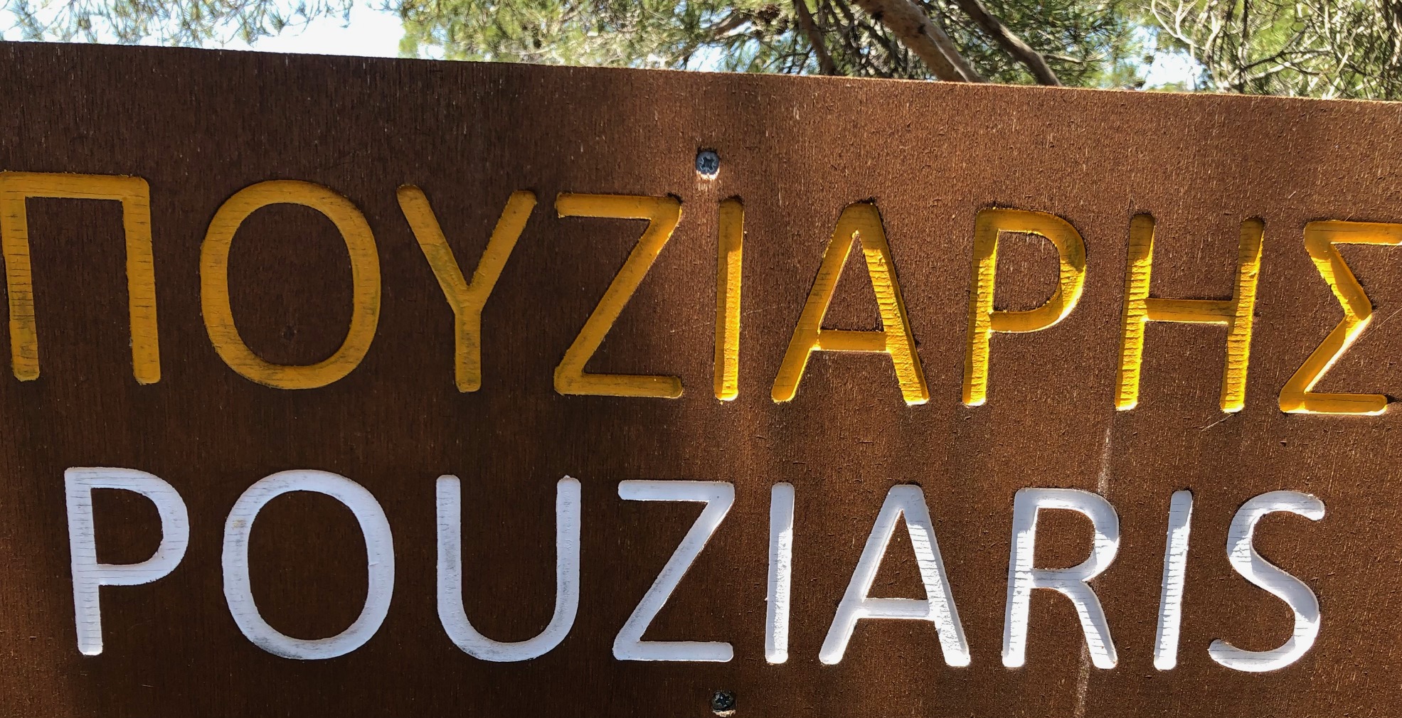 Brown wooden trail sign reading Pouziaris in Greek and English