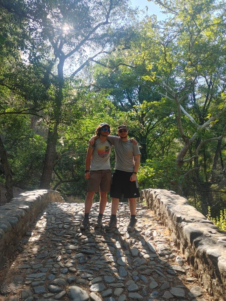 Two hikers posing on the stone Kelefos Bridge surrounded by summer trees